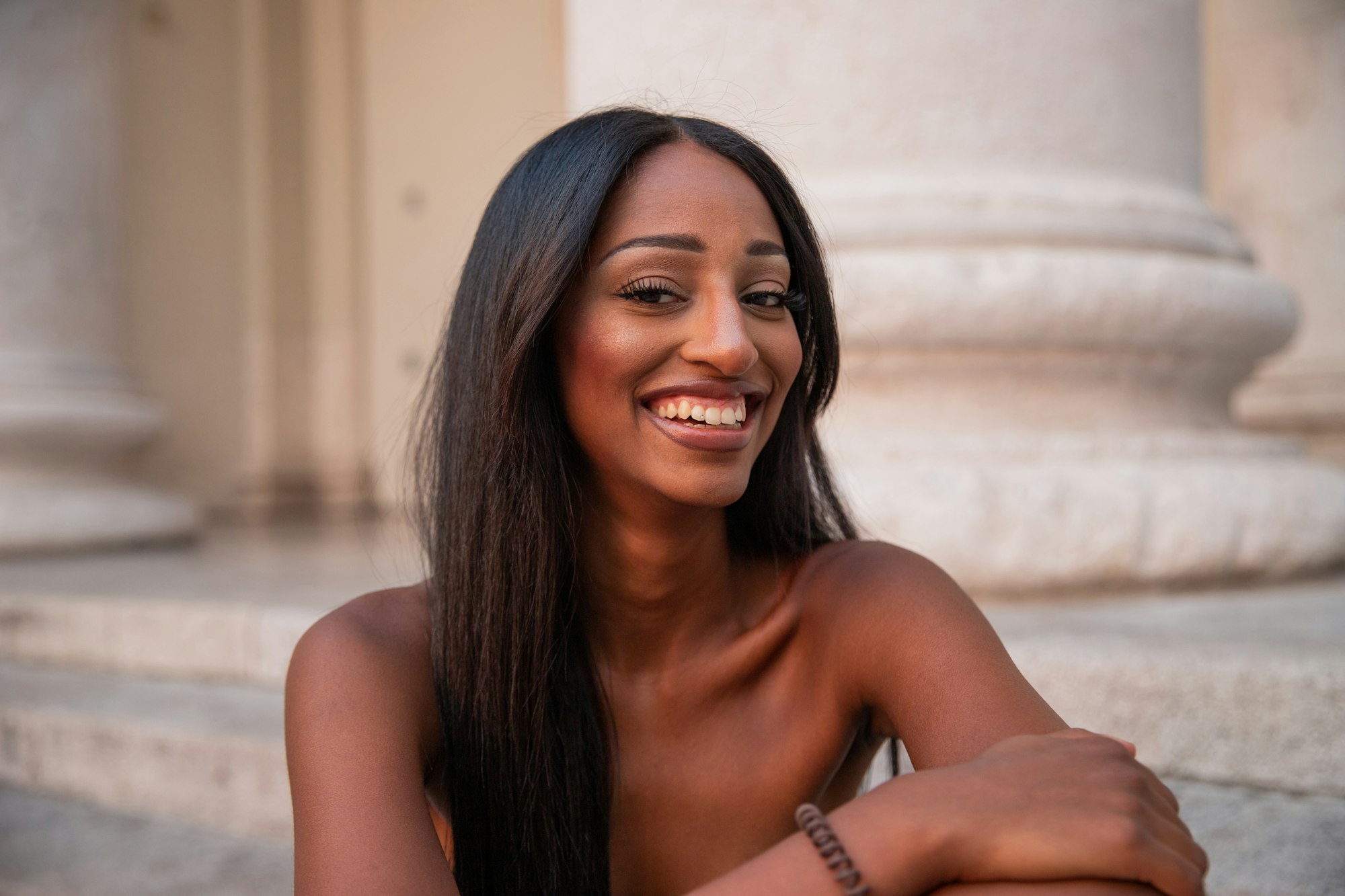 Attractive smiling young lady sitting on the stairs of a building in town